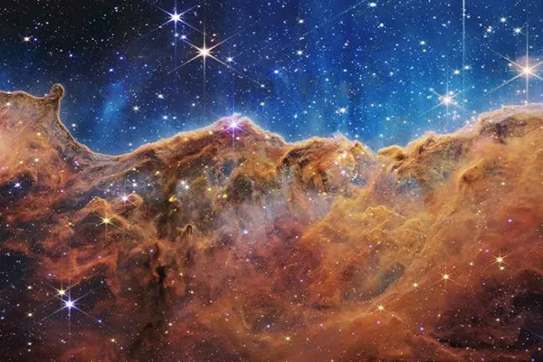 نیمه بالایی تصویر پر از ستارگان است و نیمه پایینی تصویر حاوی ستون غول‌پیکر قهوه‌ای نارنجی در سحابی کارینا است.